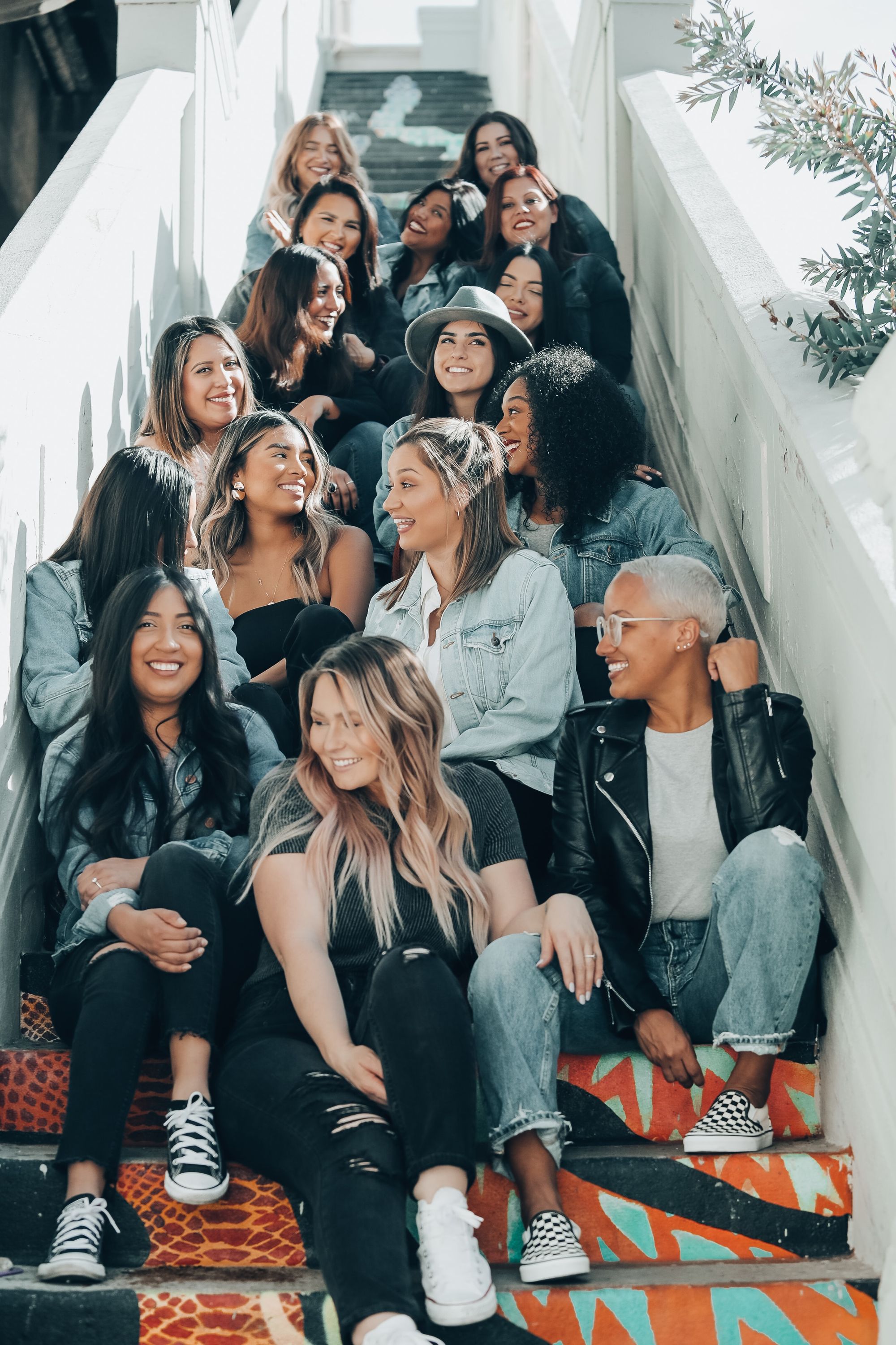 grupo composto por diferentes mulheres sentadas nos degraus de uma escada e sorrindo